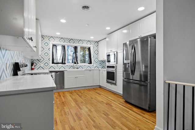 kitchen featuring sink, stainless steel appliances, backsplash, light hardwood / wood-style floors, and white cabinets