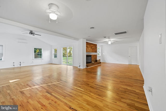 unfurnished living room with an AC wall unit, light hardwood / wood-style floors, a brick fireplace, and lofted ceiling