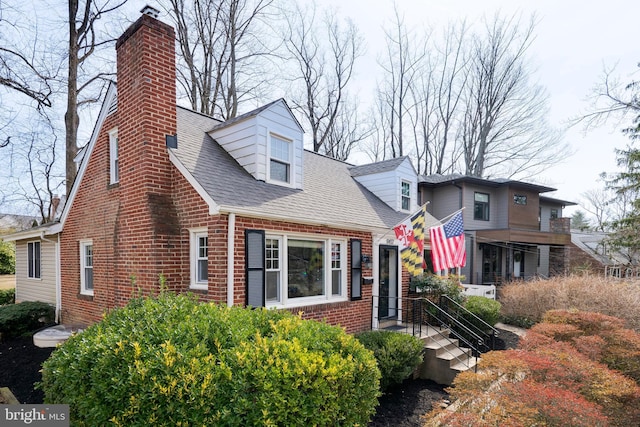 cape cod-style house featuring brick siding, a chimney, and roof with shingles