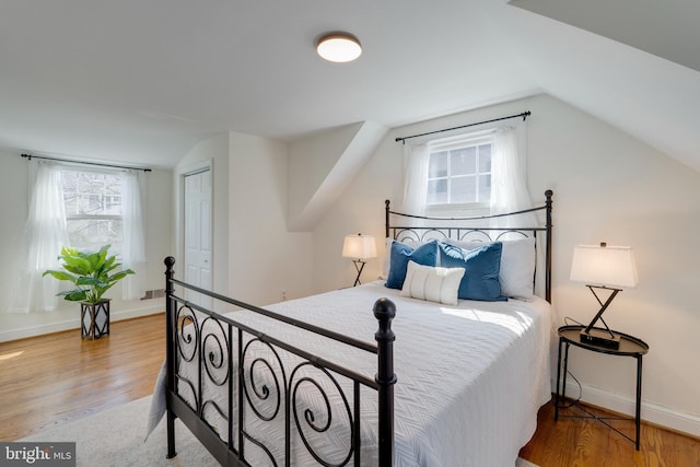 bedroom with a closet, vaulted ceiling, baseboards, and wood finished floors