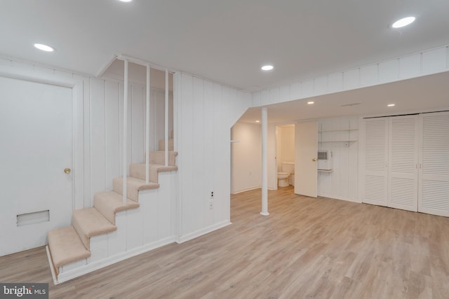 finished below grade area featuring light wood-style floors, recessed lighting, a wall mounted AC, and stairs