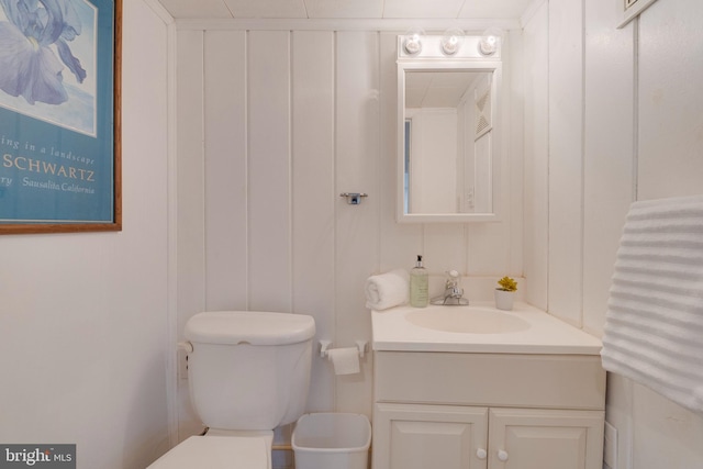 half bathroom with vanity, toilet, and a decorative wall