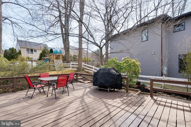 deck with outdoor dining space, a playground, fence, and grilling area