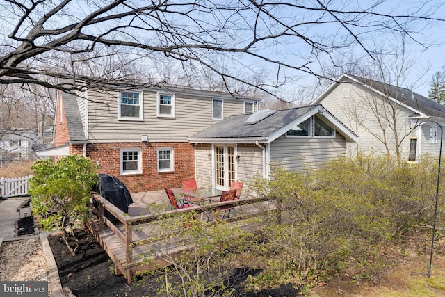 back of house featuring brick siding, roof with shingles, fence, and a wooden deck