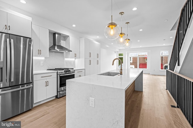 kitchen featuring stainless steel appliances, wall chimney range hood, light wood-type flooring, and a sink