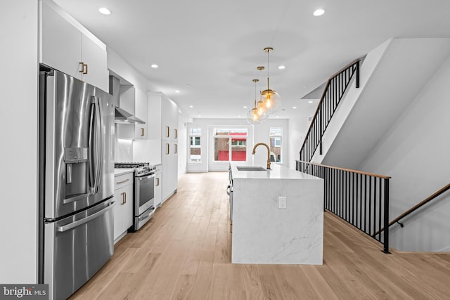 kitchen featuring pendant lighting, light countertops, appliances with stainless steel finishes, a sink, and light wood-type flooring