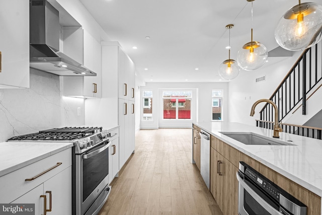 kitchen featuring light stone counters, appliances with stainless steel finishes, a sink, light wood-type flooring, and wall chimney exhaust hood