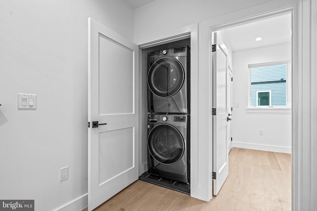 washroom with stacked washer and dryer, light wood-type flooring, laundry area, and baseboards