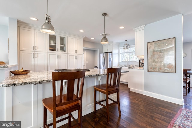 kitchen with stainless steel refrigerator, white cabinetry, light stone countertops, hanging light fixtures, and dark wood-type flooring