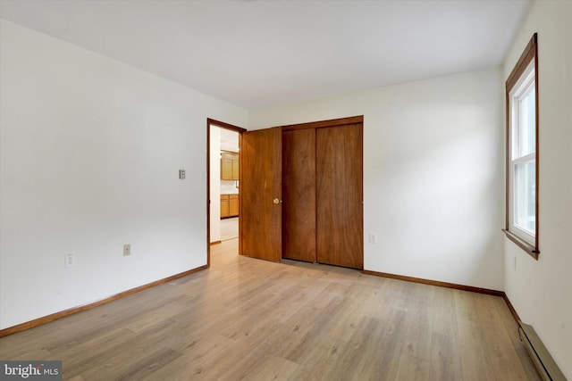 unfurnished bedroom with baseboard heating, a closet, and light wood-type flooring