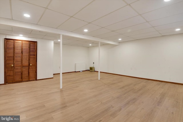 basement featuring a paneled ceiling and light hardwood / wood-style flooring