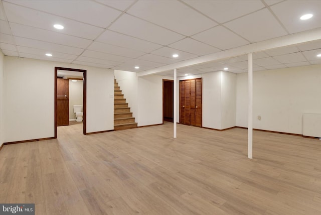 basement featuring a drop ceiling, radiator heating unit, and light hardwood / wood-style flooring