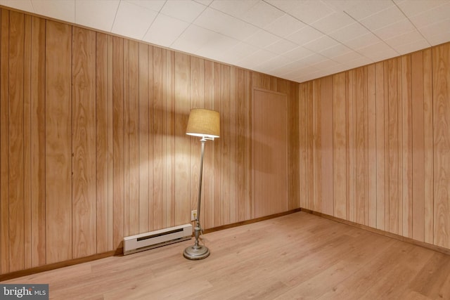 spare room featuring wooden walls, light hardwood / wood-style floors, and a baseboard heating unit