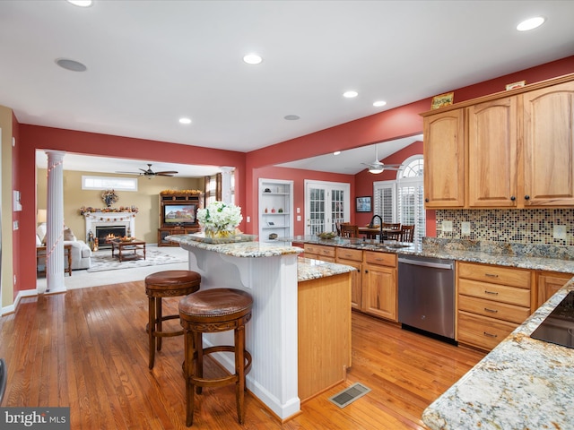 kitchen with light stone counters, a kitchen island, a kitchen bar, light hardwood / wood-style floors, and dishwasher