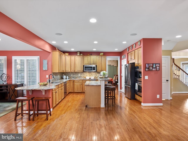 kitchen featuring kitchen peninsula, appliances with stainless steel finishes, a breakfast bar, and light wood-type flooring