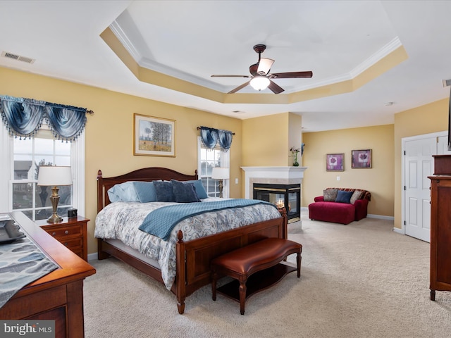 bedroom featuring light carpet, ornamental molding, ceiling fan, a tray ceiling, and a multi sided fireplace