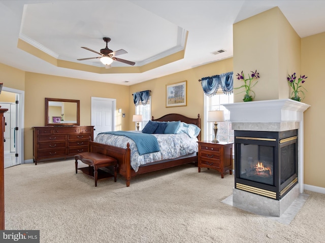 carpeted bedroom with a multi sided fireplace, ceiling fan, a raised ceiling, and ornamental molding