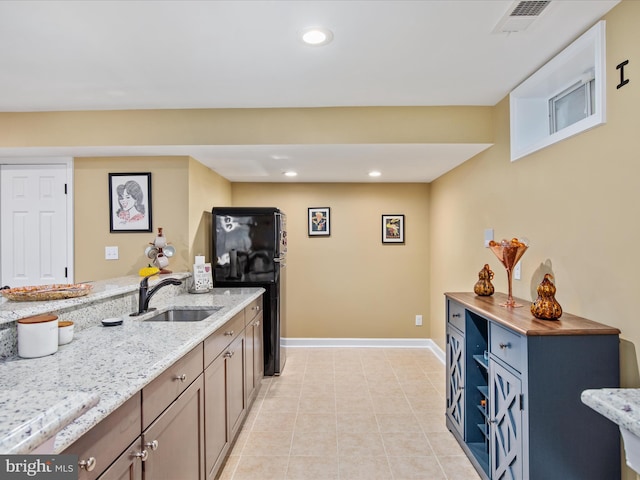 kitchen with black refrigerator, light stone countertops, sink, and light tile patterned flooring