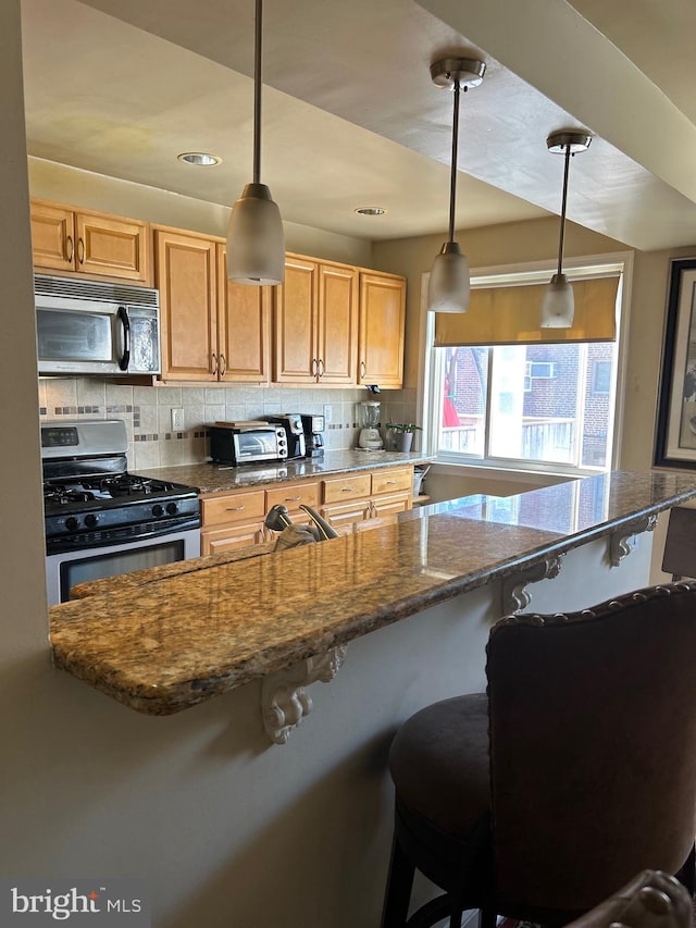 kitchen featuring appliances with stainless steel finishes, a kitchen bar, pendant lighting, and tasteful backsplash