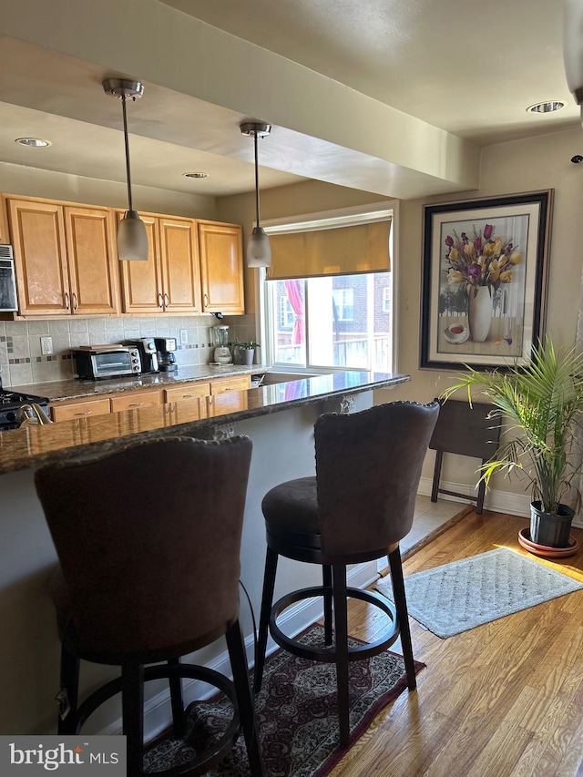 kitchen with backsplash, range, a breakfast bar area, decorative light fixtures, and light hardwood / wood-style flooring