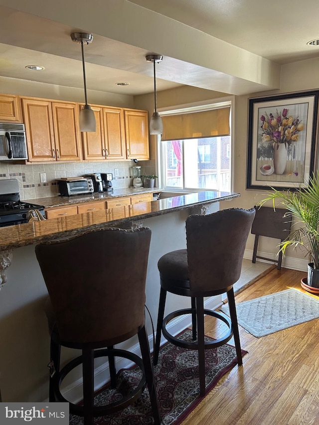 kitchen featuring a kitchen breakfast bar, tasteful backsplash, light wood-type flooring, and pendant lighting