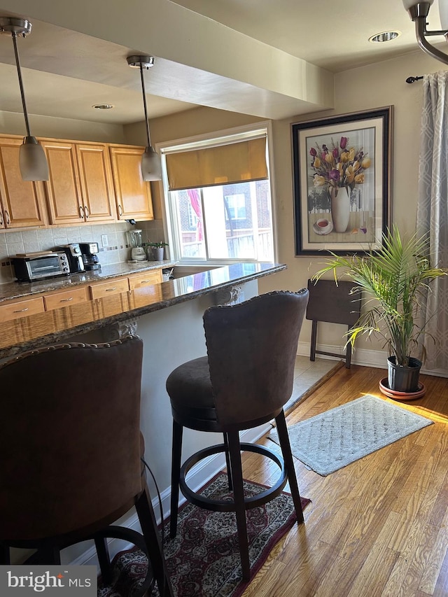 kitchen featuring a kitchen breakfast bar, dark stone counters, decorative light fixtures, light hardwood / wood-style floors, and tasteful backsplash