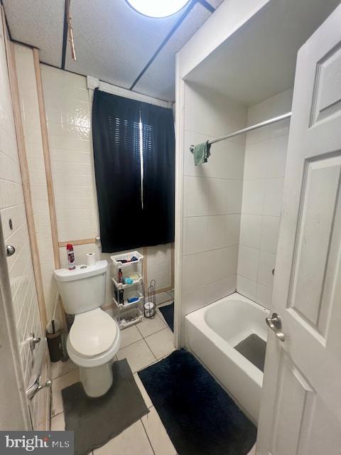 bathroom with tiled shower / bath combo, toilet, and tile patterned flooring