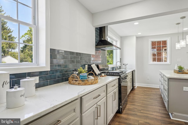 kitchen featuring wall chimney range hood, stainless steel gas stove, dark wood-type flooring, a wealth of natural light, and decorative light fixtures