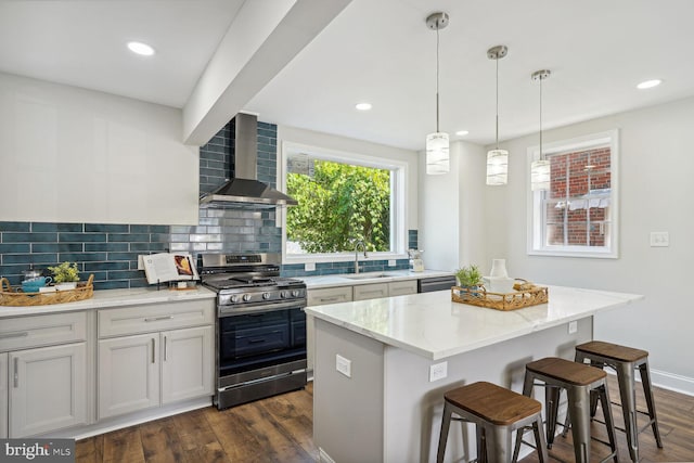 kitchen featuring wall chimney range hood, dark wood-type flooring, sink, a center island, and stainless steel range with gas stovetop