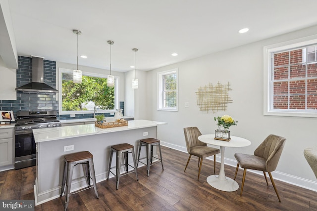 kitchen with wall chimney range hood, hanging light fixtures, stainless steel gas range, a center island, and dark hardwood / wood-style flooring