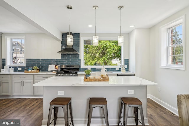 kitchen featuring wall chimney exhaust hood, stainless steel gas stove, light stone countertops, and dark hardwood / wood-style flooring