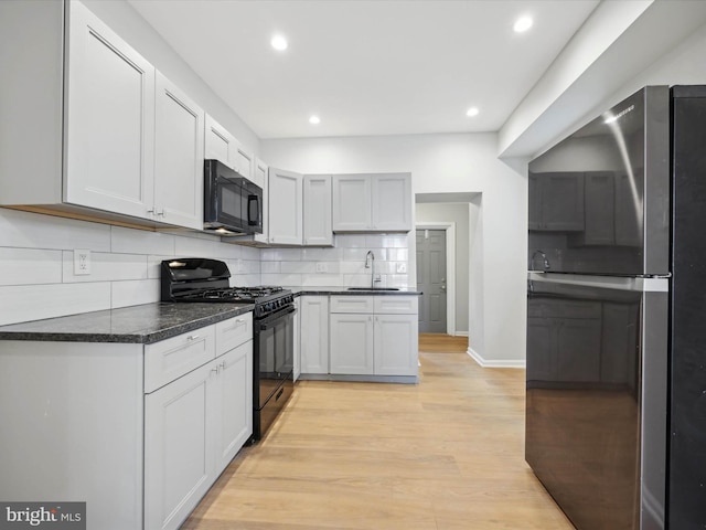 kitchen featuring white cabinets, decorative backsplash, black appliances, sink, and light hardwood / wood-style flooring