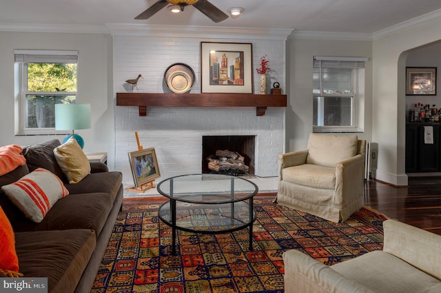 living room with crown molding, ceiling fan, a brick fireplace, and dark hardwood / wood-style flooring