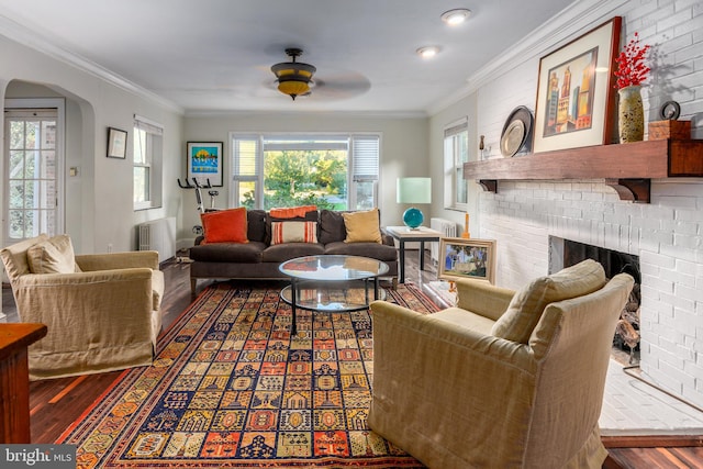 living room with crown molding, radiator heating unit, a brick fireplace, and hardwood / wood-style floors