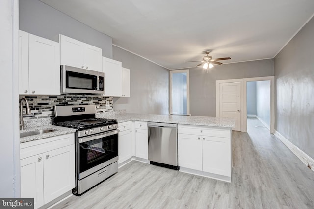 kitchen with light wood-style flooring, a sink, a peninsula, backsplash, and stainless steel appliances