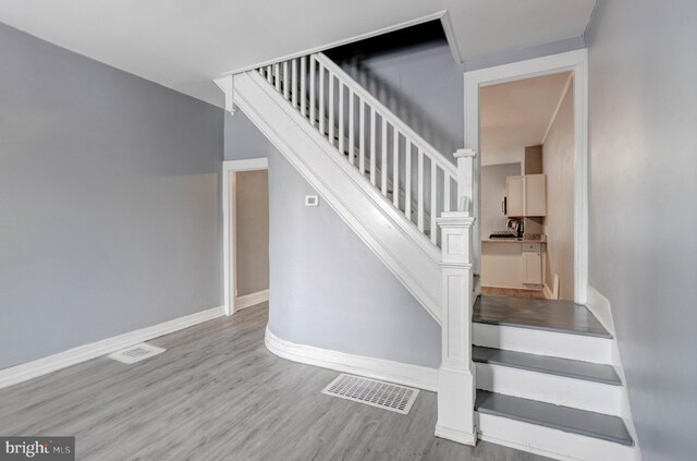 staircase with baseboards, visible vents, and wood finished floors