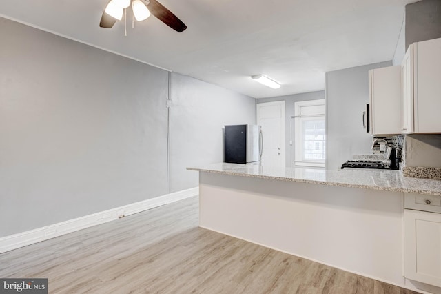 kitchen with freestanding refrigerator, a ceiling fan, light wood-style flooring, light stone counters, and a peninsula