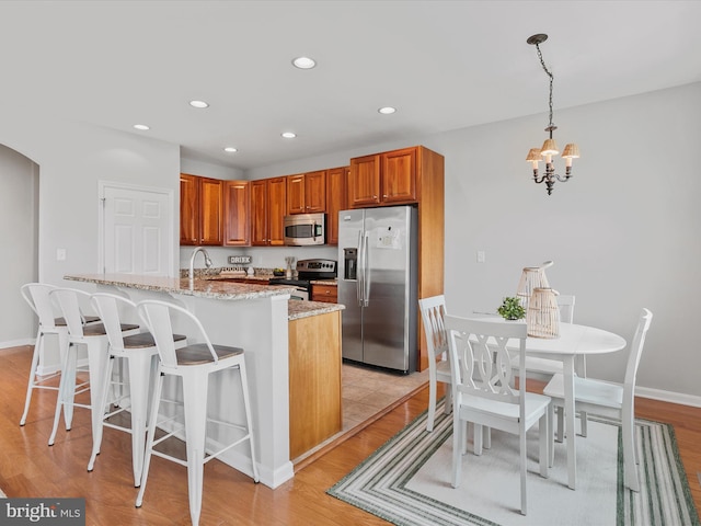 kitchen featuring light wood-type flooring, stainless steel appliances, pendant lighting, light stone counters, and a notable chandelier