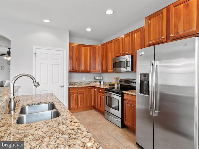 kitchen with sink, light stone countertops, light tile patterned floors, appliances with stainless steel finishes, and ceiling fan