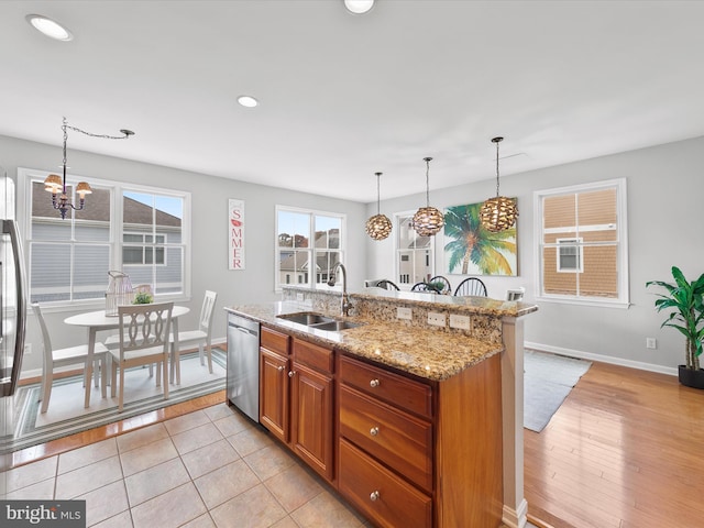 kitchen with sink, hanging light fixtures, light hardwood / wood-style floors, stainless steel dishwasher, and a kitchen island with sink