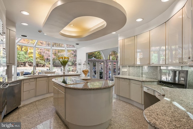 kitchen featuring a center island, a raised ceiling, sink, stainless steel dishwasher, and light stone countertops