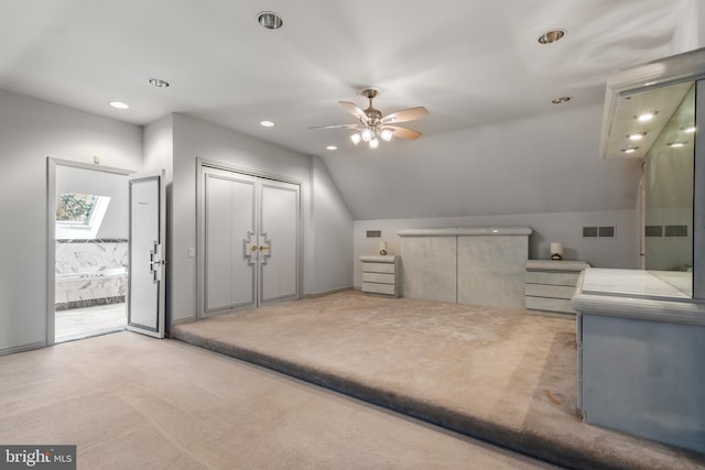 unfurnished bedroom featuring light colored carpet, ceiling fan, and vaulted ceiling with skylight