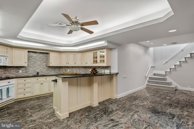 kitchen featuring white appliances, a raised ceiling, sink, decorative backsplash, and cream cabinetry