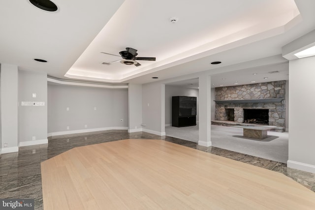 unfurnished living room featuring a raised ceiling, ceiling fan, a fireplace, and wood-type flooring