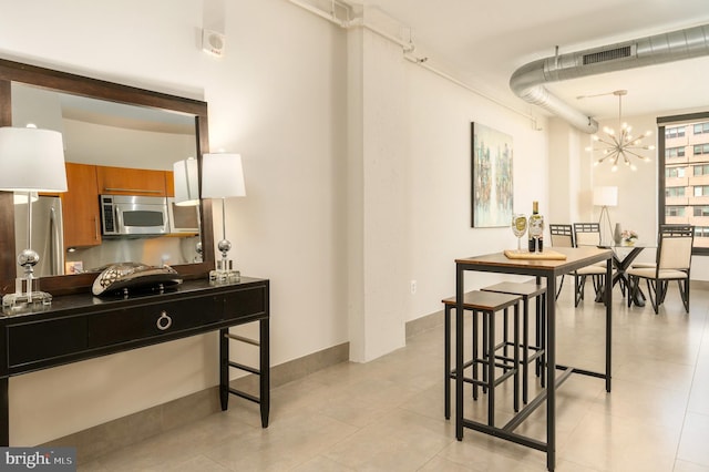 interior space featuring appliances with stainless steel finishes, an inviting chandelier, a breakfast bar area, and light tile patterned flooring