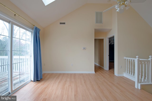 empty room with ceiling fan, high vaulted ceiling, a skylight, and light hardwood / wood-style flooring