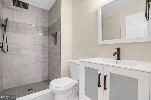 bathroom featuring a tile shower, toilet, and vanity