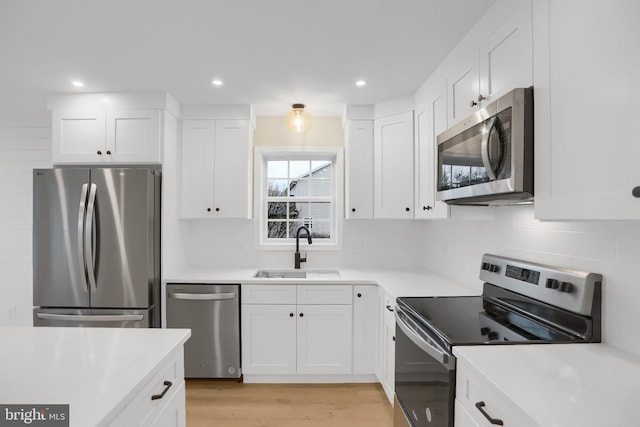 kitchen featuring stainless steel appliances, sink, light wood-type flooring, white cabinetry, and tasteful backsplash