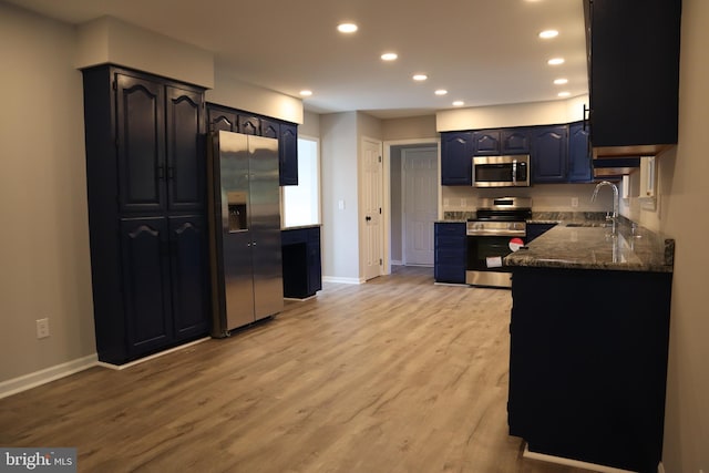 kitchen with stainless steel appliances, dark stone countertops, light hardwood / wood-style floors, and sink