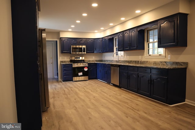 kitchen featuring stainless steel appliances, light hardwood / wood-style floors, dark stone counters, and sink